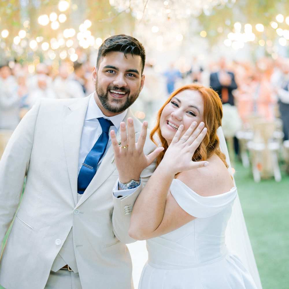 Our customers George and Skye holding up their wedding rings and smiling at the end of the aisle.