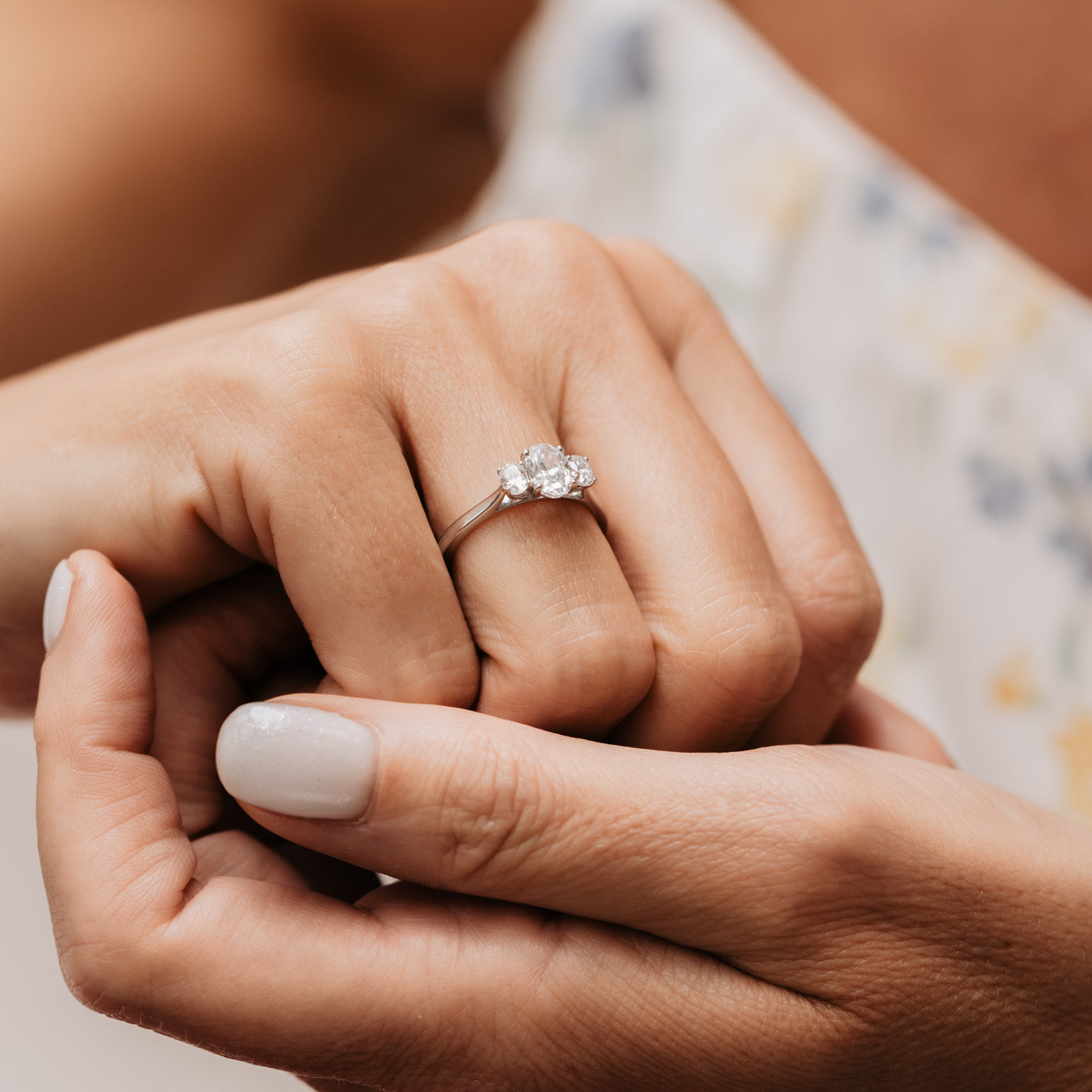 Cinta oval trilogy ring worn on models hand with models white flowery dress in background..