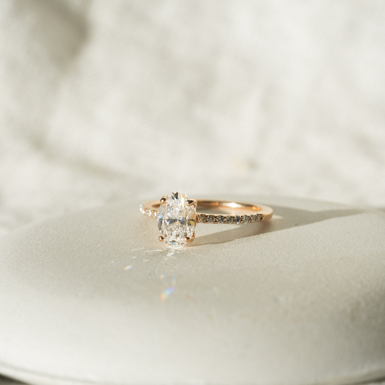 Oval shoulder set lab-grown diamond engagement ring on a white dish