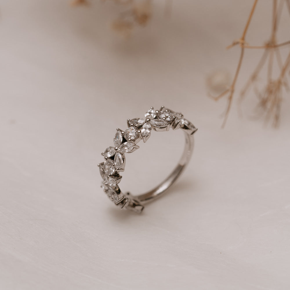 Close up of floral multistone lab diamond ring balanced upwards on a white background with soft dried flowers.