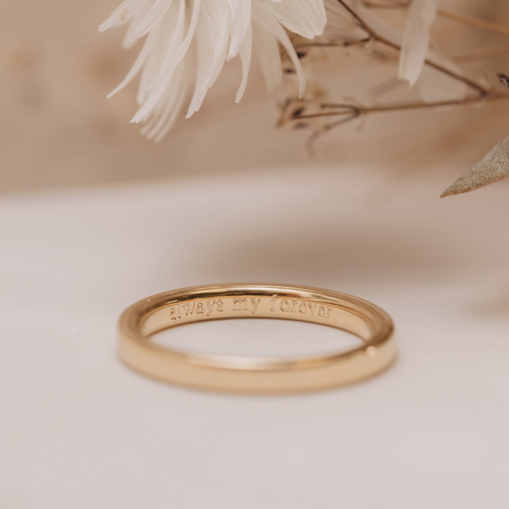 Photograph of plain gold wedding band with 'Always My Forever' engraved on the inside.
