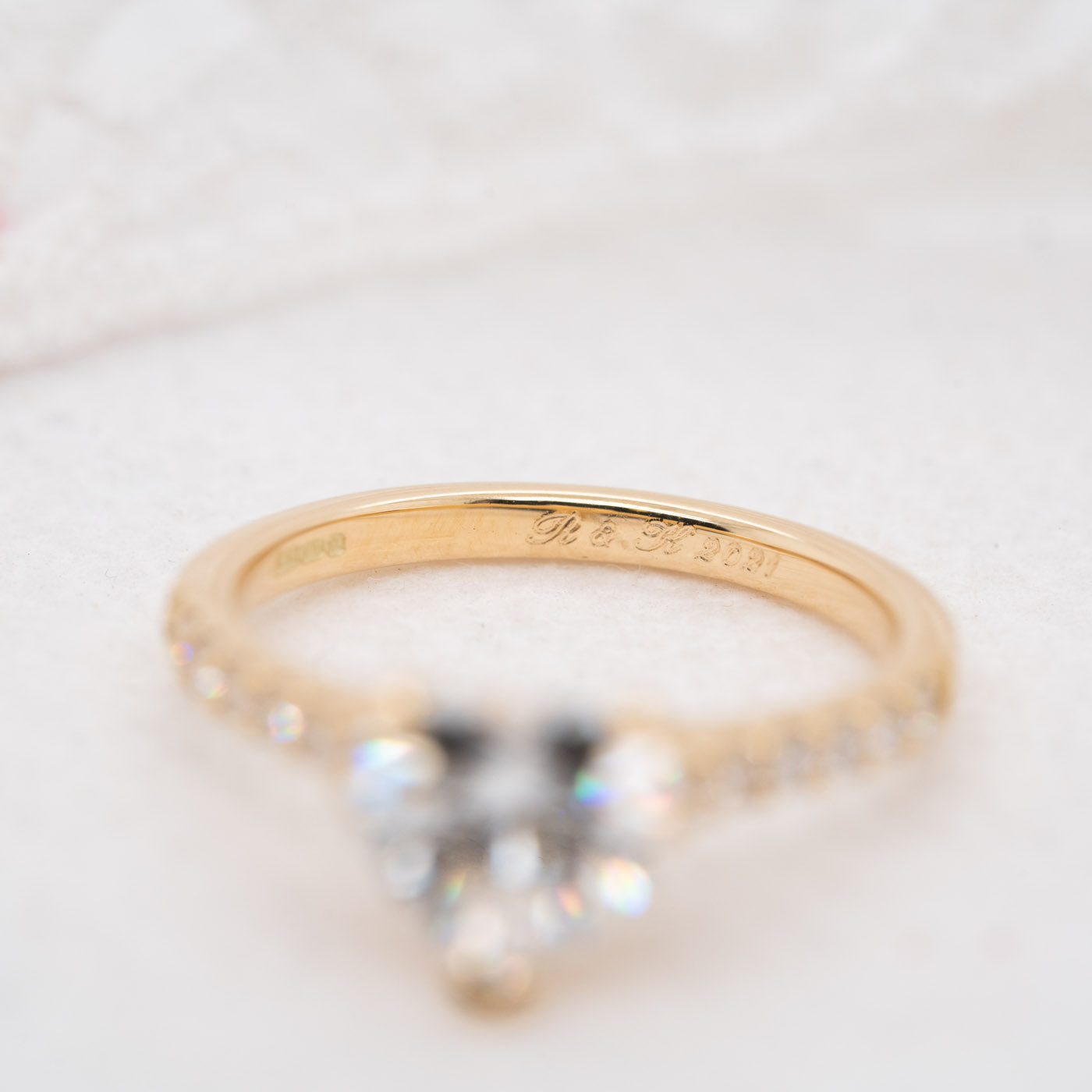 Close up photograph of a gold engagement ring with initial and the date engraved in script font on the inside of the band.