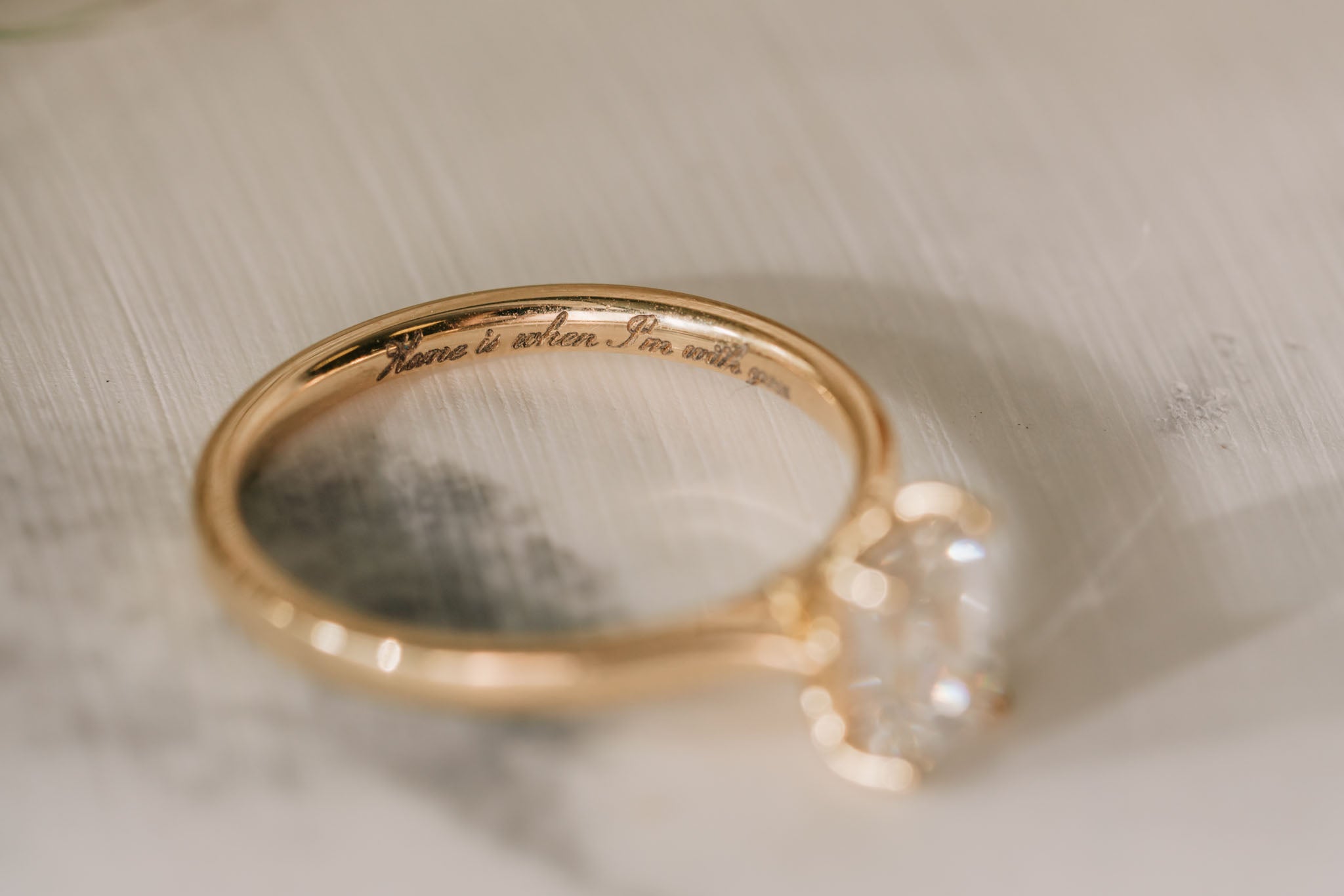 Close up image of gold ring with 'Home is where i'm with you' engraved in script font on the inside of the band.