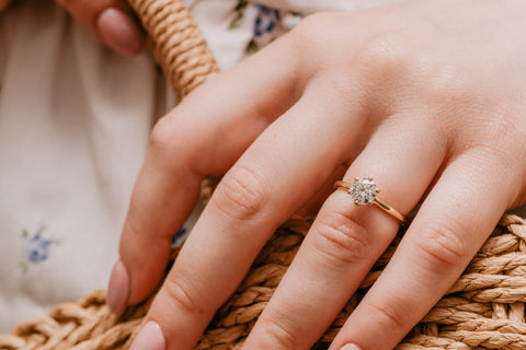 Model's hand wearing a gold and lab grown diamond engagement ring with a wicker rope background