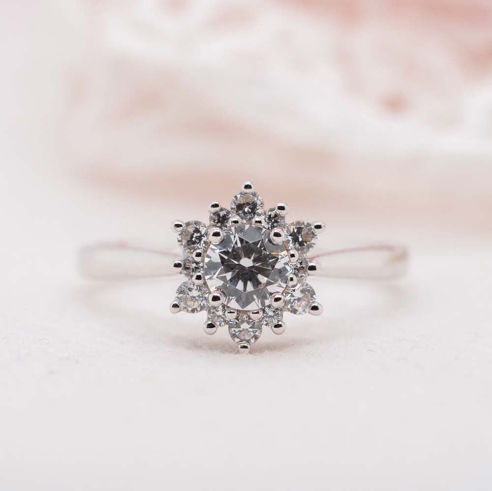 Close up of the front of flower inspired halo engagement ring in platinum, on a white lace background.