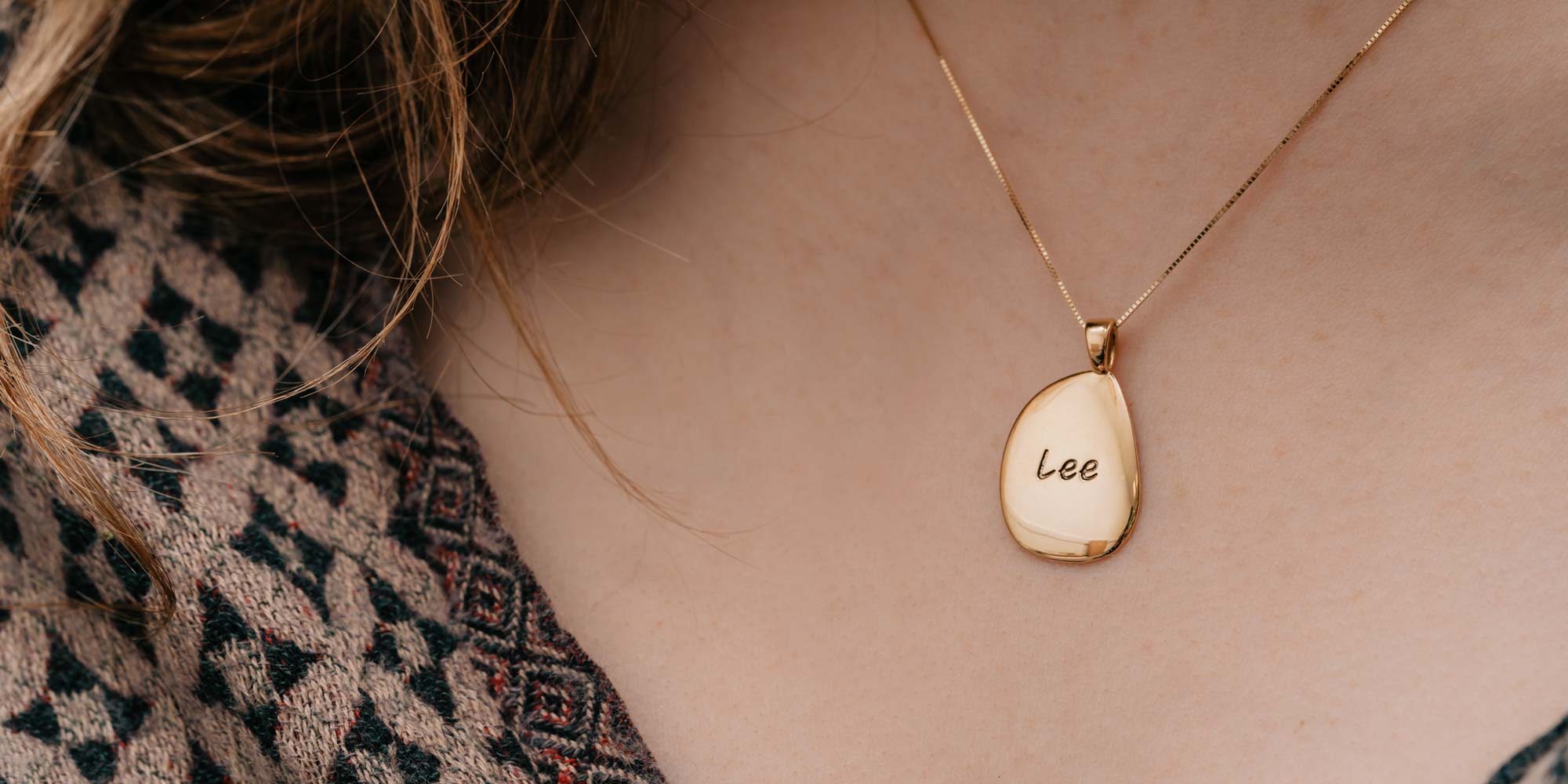 Gold pebble necklace engraved with 'Lee' worn on models neck.