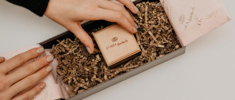 close up of packaging, ring box being placed delicately into a postal box with branded tissue paper