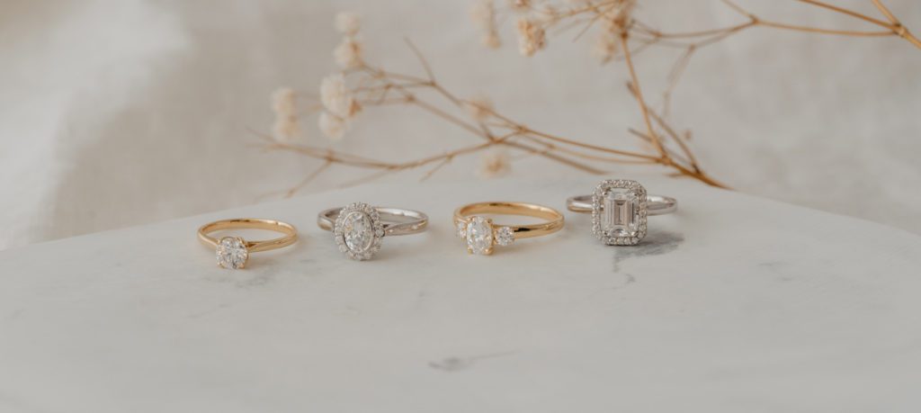 Four rings in various metals with plants in the background surrounded by white cloth