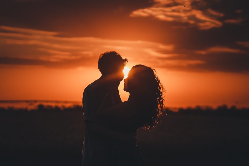 The silhouette of a couple embracing agains a striking orange sunset.