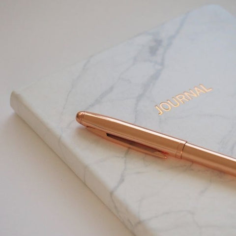 A marble journal resting on a work desk with a gold pen