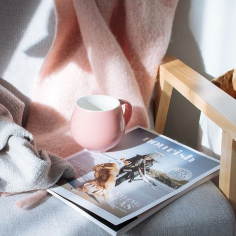 A pink coffee mug resting on a magazine on rocking chair