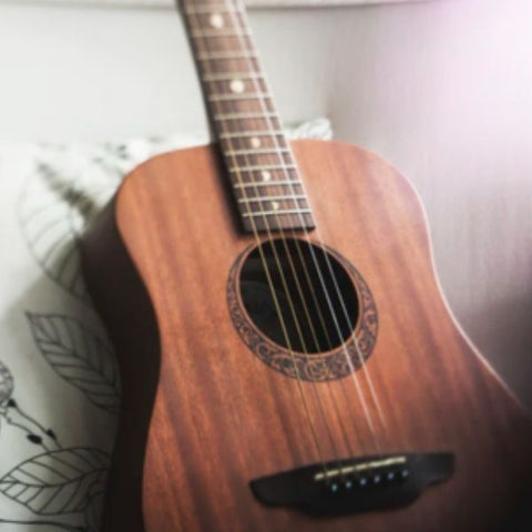 Image of a brown acoustic guitar leaning on a while pillow on a desk chair