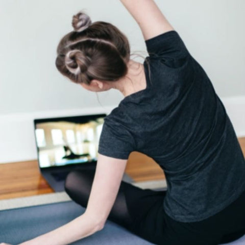 Image: Woman practicing stretches in front of her laptop, watching a live workout