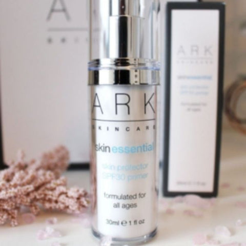 Product image of ARK Skincare's Skin Essential SPF 30 Primer next to it's product box on a white counter top with pretty pink crystals scattered around it.
