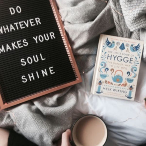 Image of a flat lay on a cosy duvet with a cup of tea, book and a candle