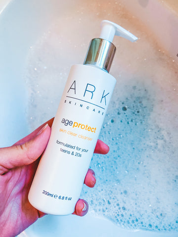 Product Image: ARK Skincare's Age Protect Vitality Cleanser held over a bubble bath