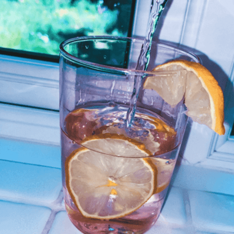 Image: Water pouring into a pink glass with slices of lemon 