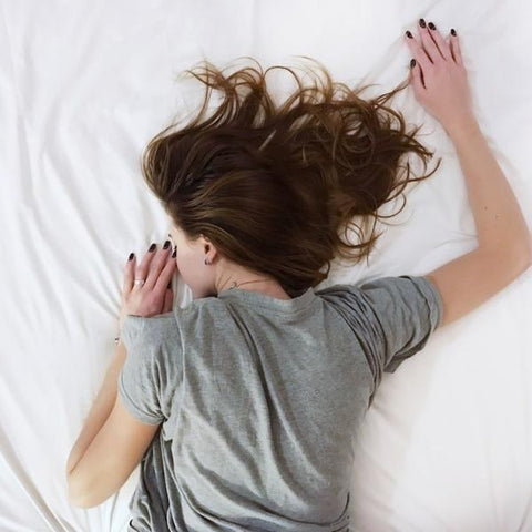 Young woman lying on a white bedsheet asleep