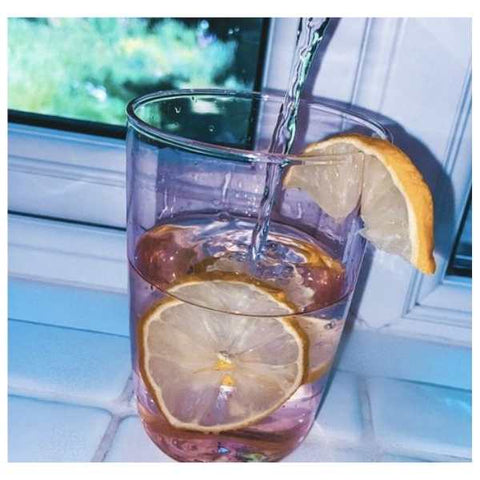 Image: water being poured into a pink glass with ice and lemon. 