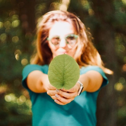 young woman walking through the woods holding out a green leaf to represent vegansim