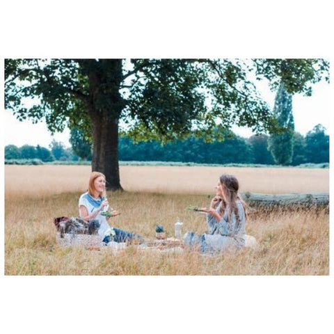 Image: Two ladies sat on a picnic blanket in a corn field 