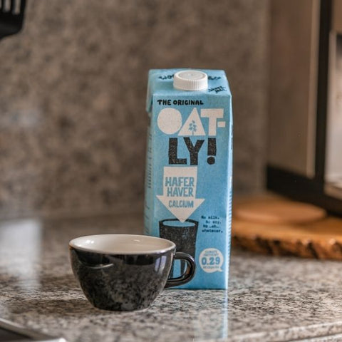 A carton of oat milk from Vegan brand Oat-ly! next to a coffee cup. 