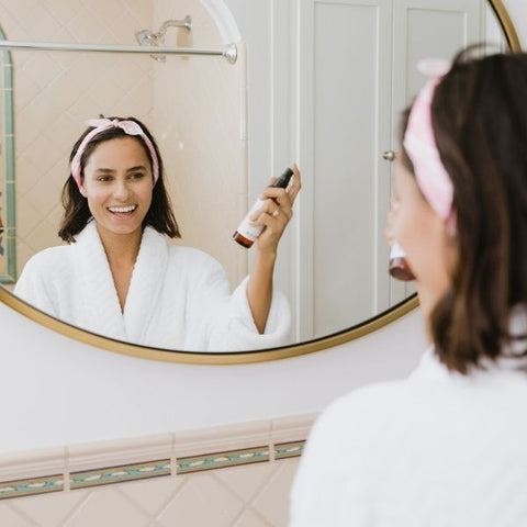 Woman applying her skincare products in front of a bathroom mirror