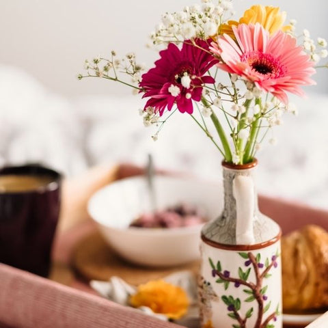 A vase of flowers on a breakfast tray with cereal and pastries