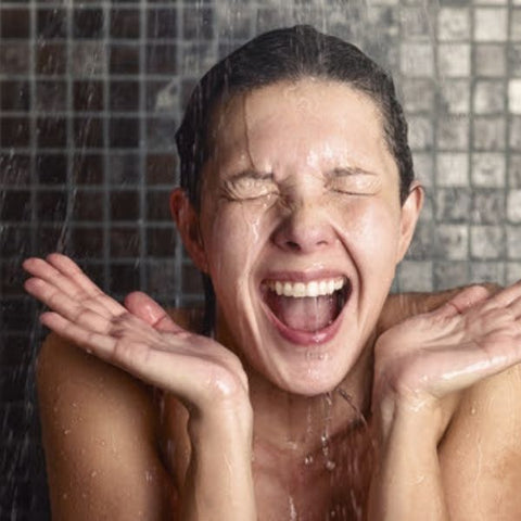 A woman laughing and looking shocked as she showers in cold water