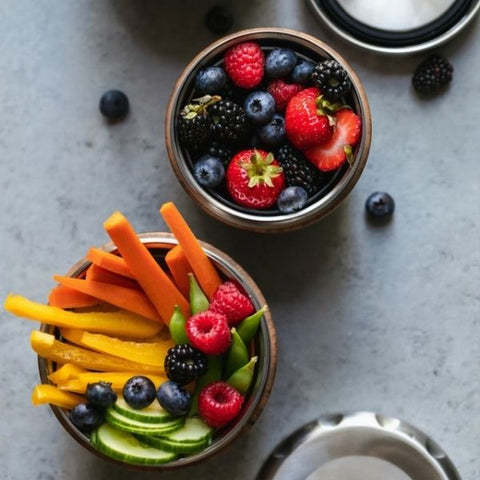 Two pots of different healthy snacks including carrot and pepper sticks and mixed berries