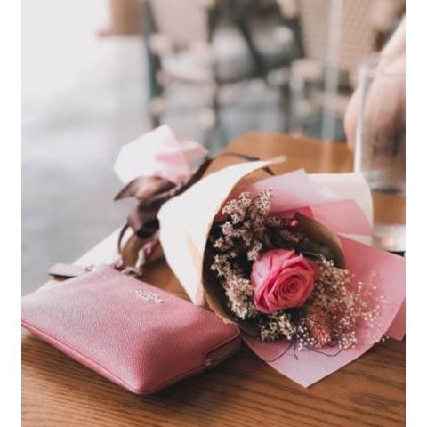 Image: Pink roses wrapped up in tissue paper next to a purse laid on a wooden table