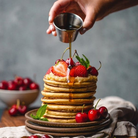 Stack of vegan pancakes with berries drizzled in maple syrup 