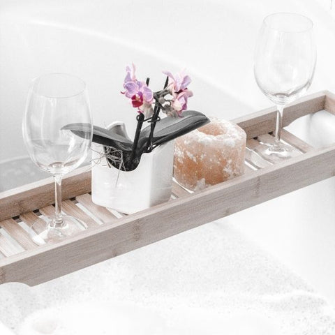 A wooden bath tray laid across a white bath tub holding a small flower and glass of wine