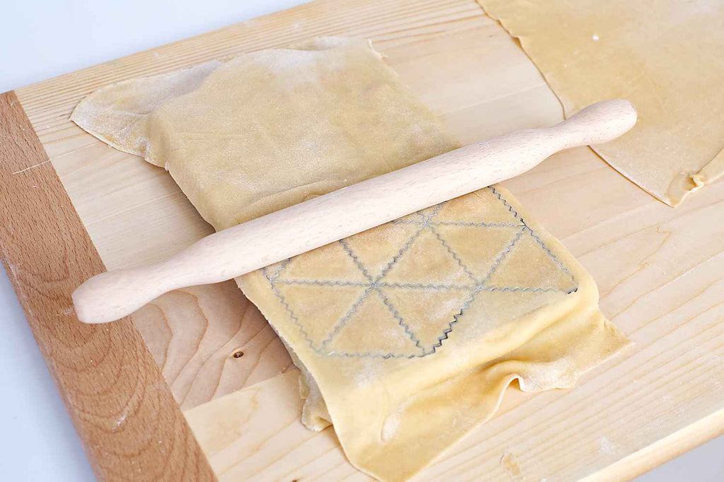 Cutting ravioli shapes on the tray using a rolling pin.