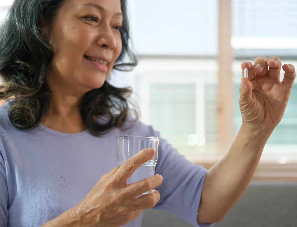 woman holding a glass of water and a supplement capsule