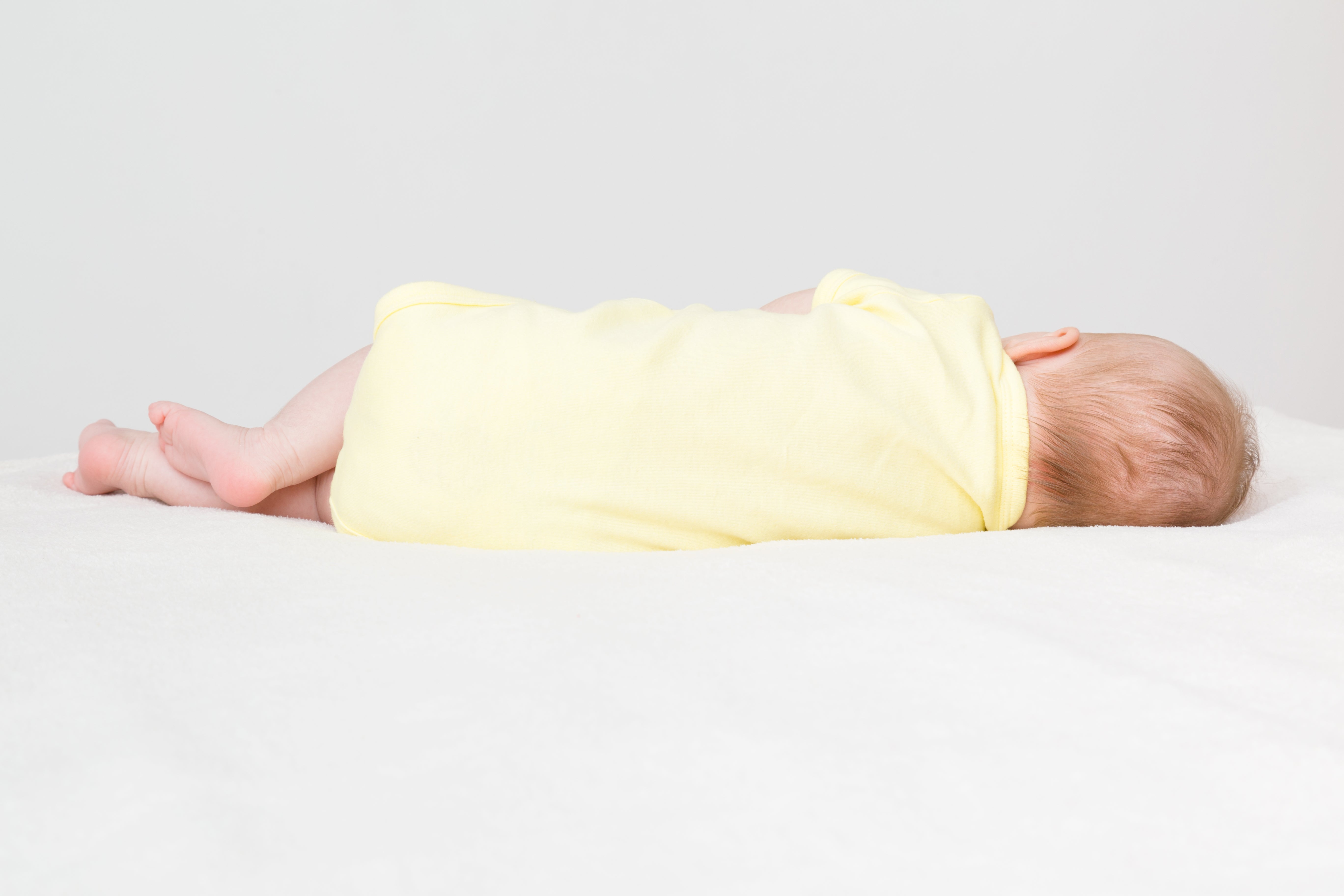 Image of young baby sleeping on their side in yellow romper