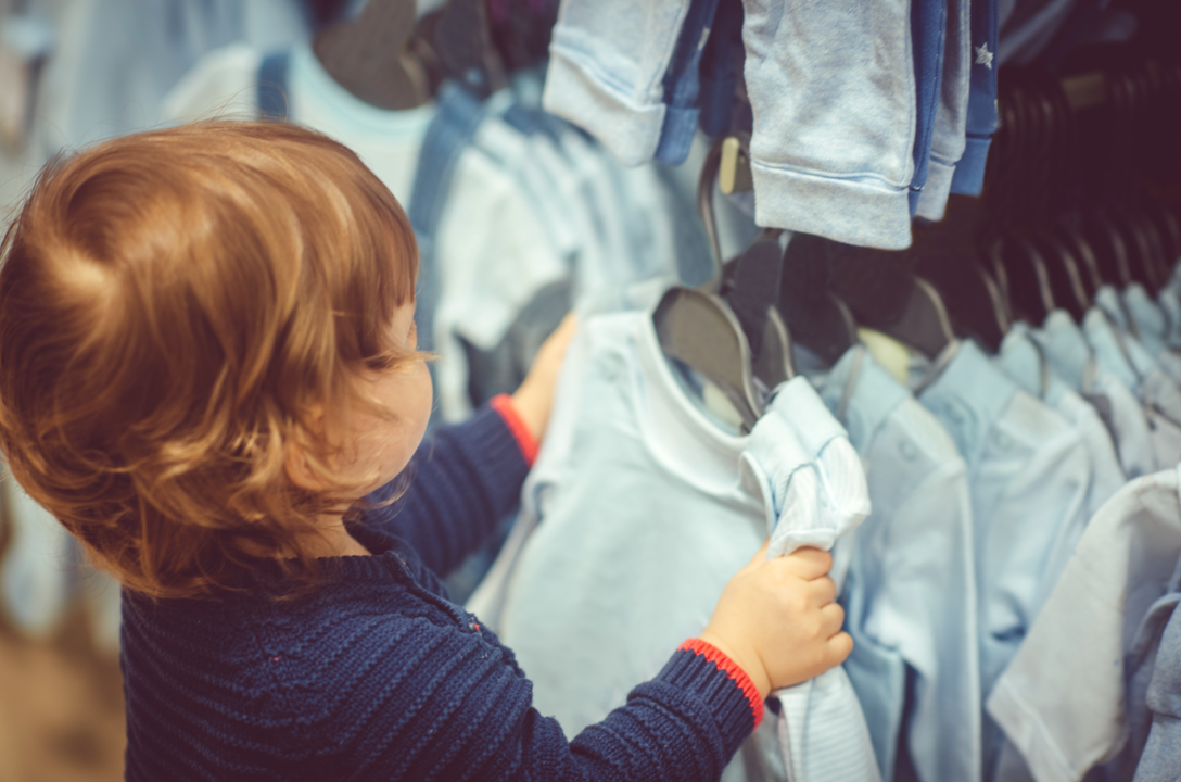 Young boy examining different clothing products in shop including cotton baby sleep sacks