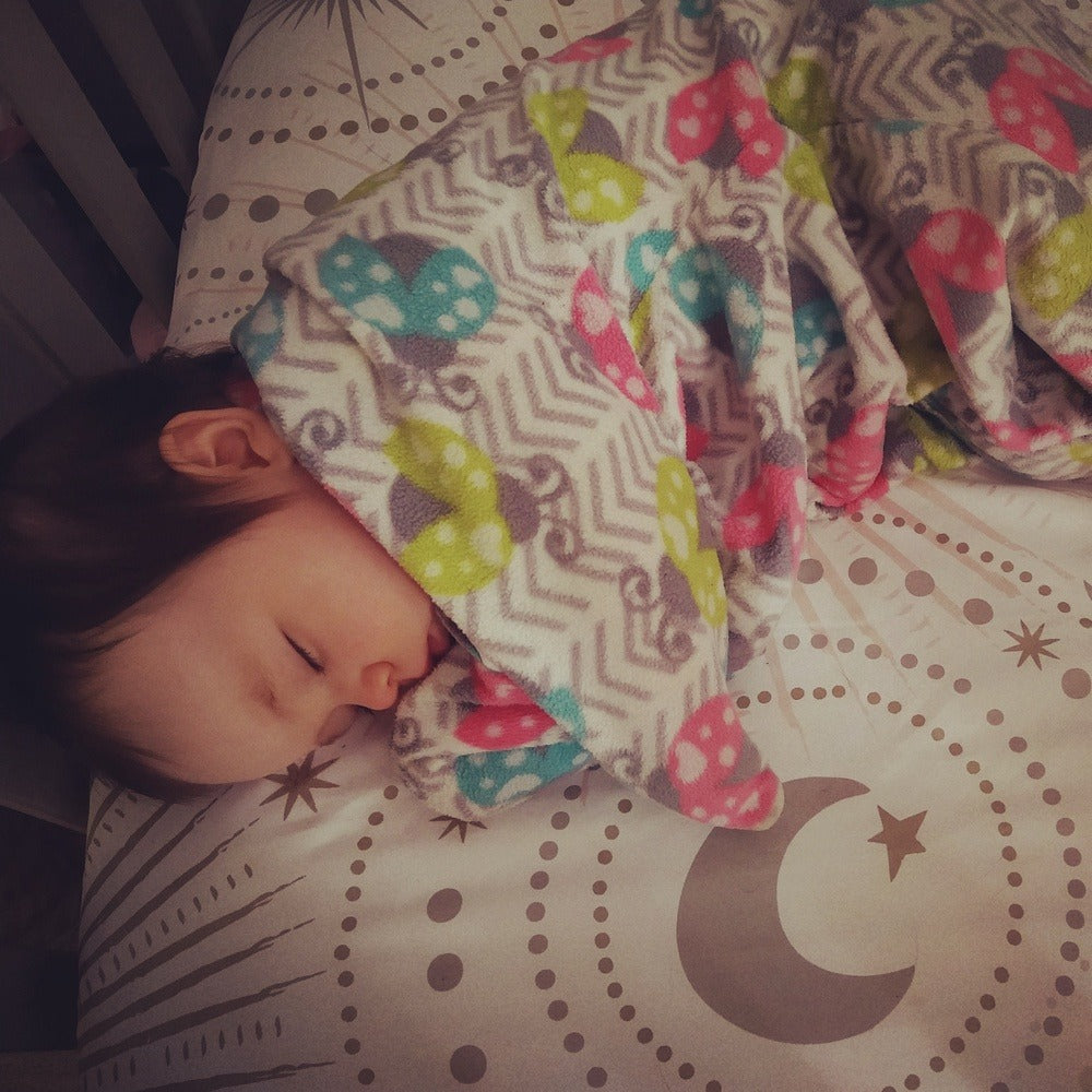 View of young infant through crib bars sleeping safely on her back