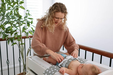 A baby is lying on a change table, wrapped in a WriggleBum nappy change harness. His mum is adjusting the fit of his cloth nappy.