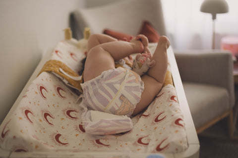 A baby in a nappy is lying on a change table with their legs in the air.