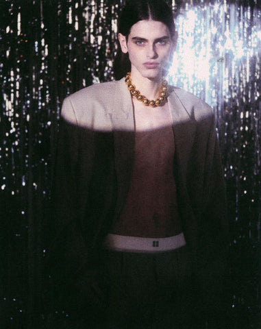 Individual with long, dark hair standing in gold ball necklace from Ben-Amun with open, oversized blazer against silver streamers