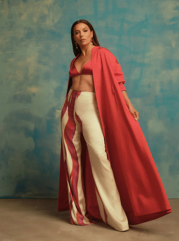 Eva Longoria standing in red and cream outfit against blue background