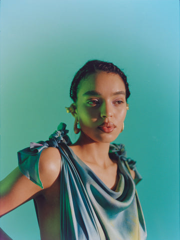 Woman in blue draped shirt posing against blue background in Ben-Amun earrings