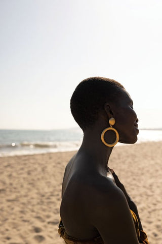 Close-up of Achok Majak wearing circular gold hammered earrings on the beach