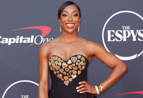 Ego Nwodim wearing sweetheart cut black dress with gold embellishments, gold bangles, and gold earrings in front of ESPY red carpet background