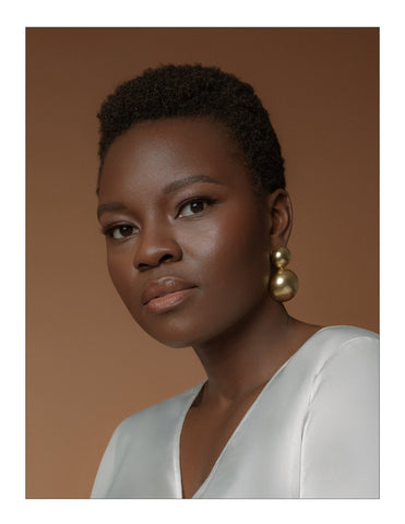 Shaunette Renee Wilson wears gold ball earrings against brown background