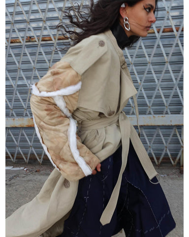 Woman walking quickly forward wearing a beige trench coat and silver chain earrings
