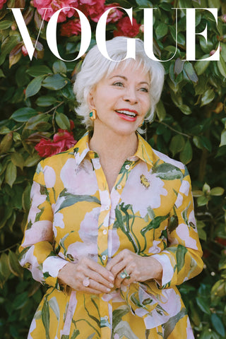 Isabel Allende wearing Ben-Amun earrings and yellow, floral dress against floral background with white Vogue logo overhead