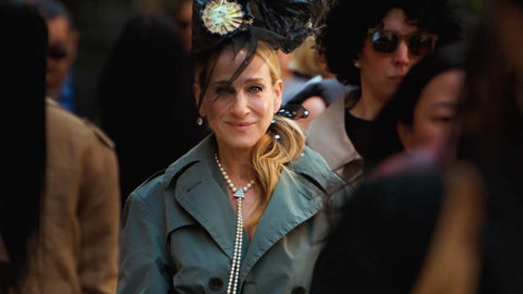 Sarah Jessica Parker wears gray coat and black hat with Ben-Amun long pearl necklace as she walks on a crowded sidewalk