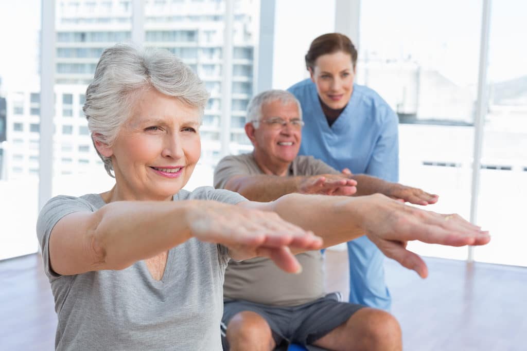 Female therapist assisting senior couple with exercises in the medical office